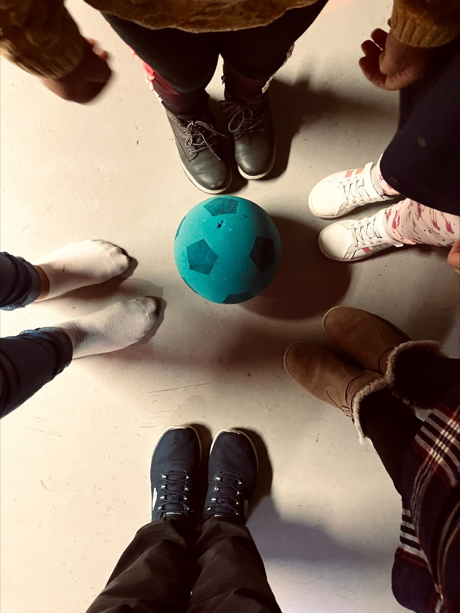 fünf Paar Füße sind von oben fotografiert. In der Mitte liegt ein blauer Softball mit dunkelblauen Punkten.